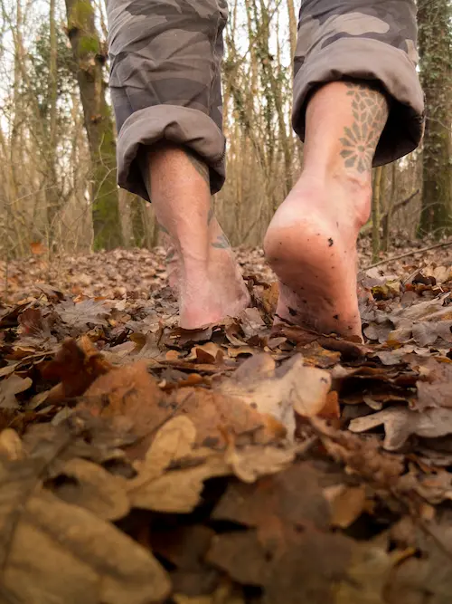 Pieds d'un homme sur des feuilles dans la forêt. Marcher pieds nus favorise l'ancrage