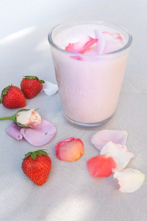 Verre de smoothie sur une table, autour des pétales de rose et quelques fraises