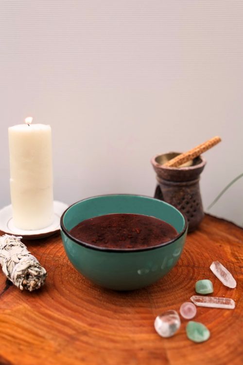 bol de cacao sacré avec autour une bougie, un bâton de sauge et des cristaux, posés sur une table en bois